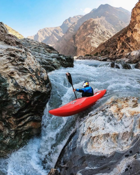 In this picture taken off Go Pro's Instagram account there is a person in a blue jacket in a red kayak going down some rapids. In the background of the image there are mountains and a blue sky. Building an online presence.